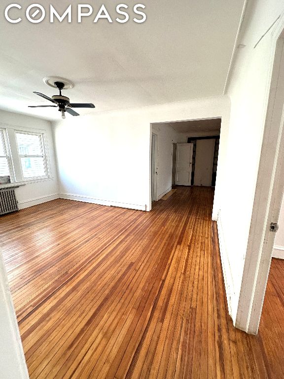 unfurnished room with ceiling fan, radiator, and wood-type flooring