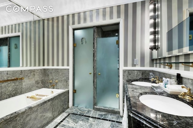 bathroom featuring a sink, a wainscoted wall, a garden tub, and wallpapered walls