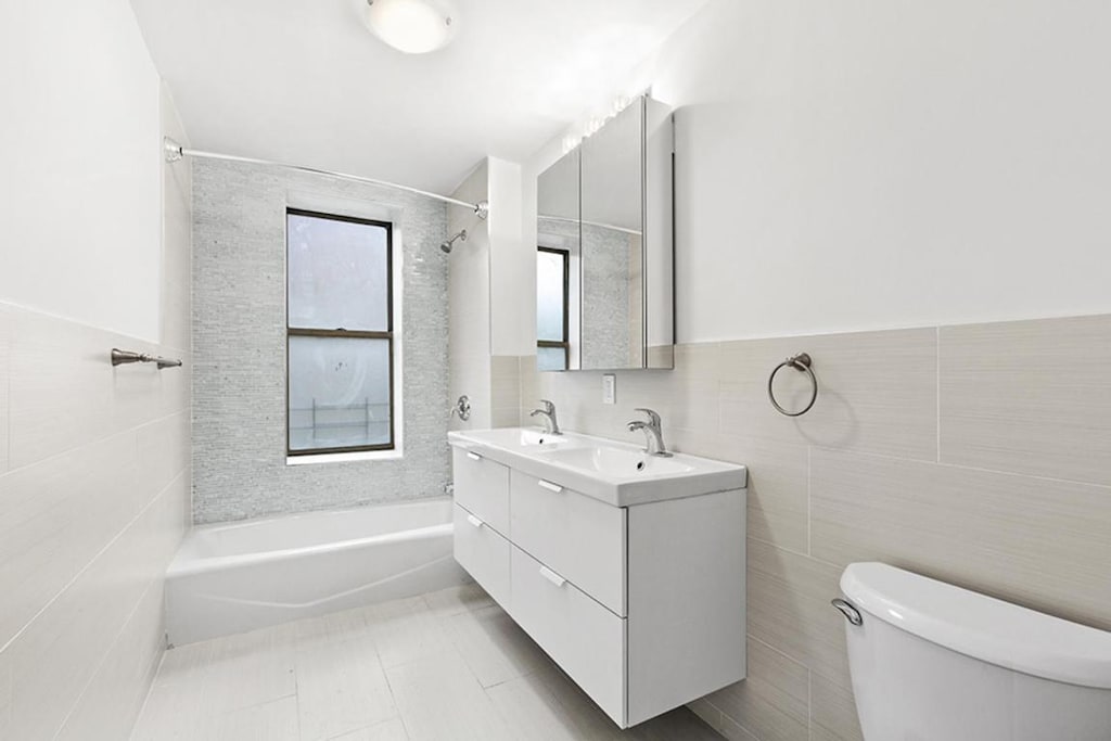 full bathroom with tile walls, vanity, tiled shower / bath, and toilet