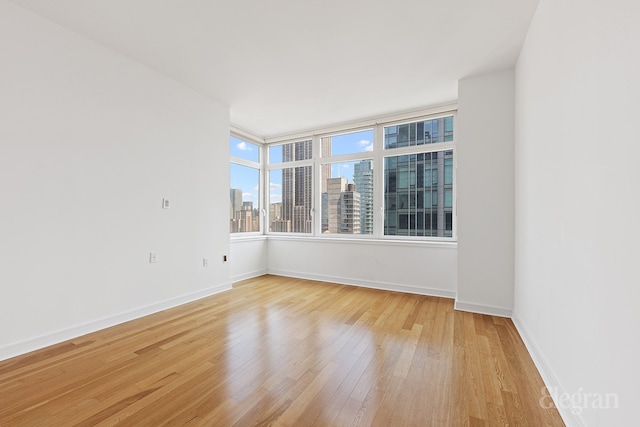 empty room featuring a view of city, light wood-style flooring, and baseboards