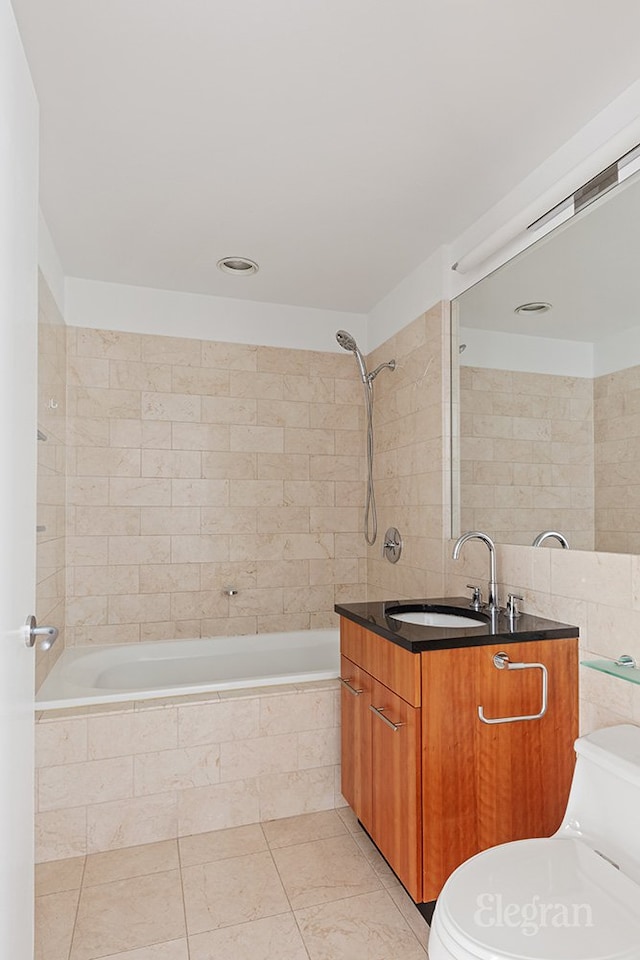 full bathroom with toilet, tiled shower / bath, tile walls, and vanity