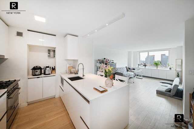 kitchen with white cabinets, stainless steel gas stove, sink, kitchen peninsula, and light hardwood / wood-style flooring