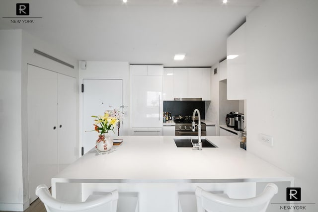 kitchen with a peninsula, white cabinets, a sink, light countertops, and a kitchen breakfast bar
