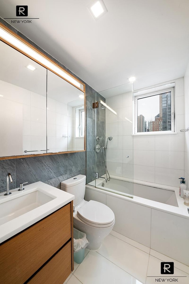 bathroom featuring tile walls, healthy amount of natural light, vanity, tile patterned flooring, and bath / shower combo with glass door