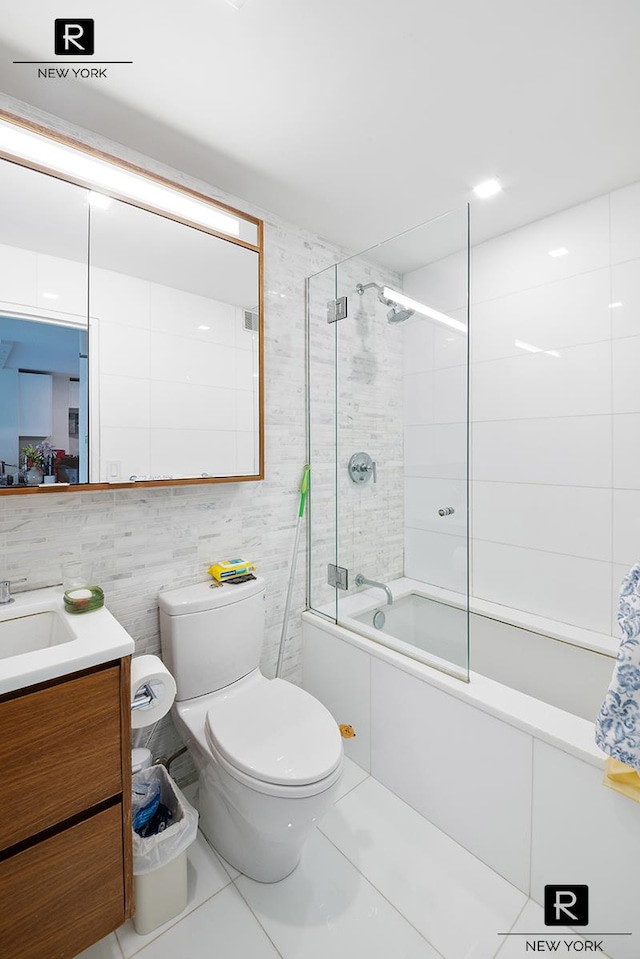 bathroom featuring tile walls, vanity, shower / bath combination with glass door, toilet, and tile patterned flooring