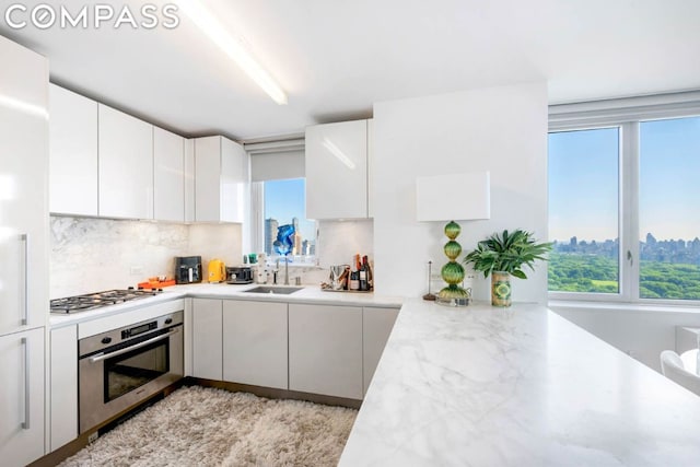 kitchen featuring light stone countertops, white cabinets, stainless steel appliances, sink, and backsplash