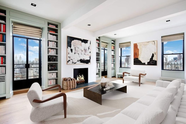 living area featuring beamed ceiling, built in features, wood finished floors, and a warm lit fireplace