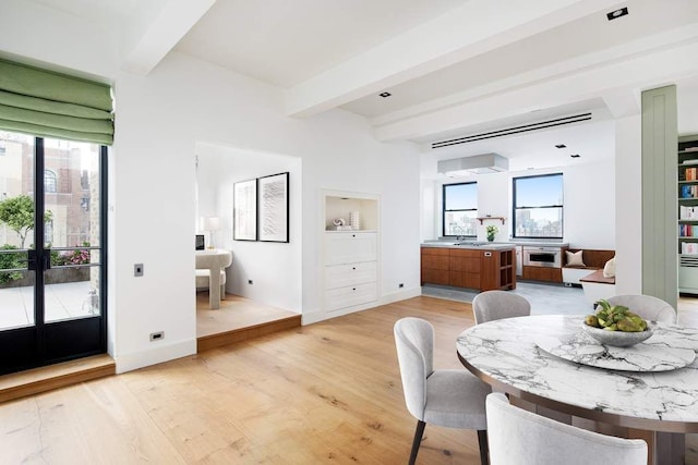 dining room with beam ceiling, baseboards, and light wood-style floors