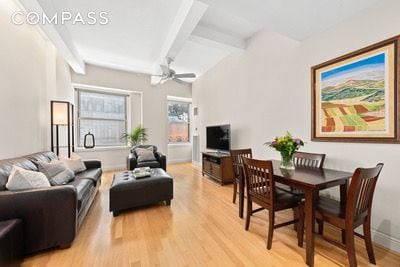 living room featuring beam ceiling, ceiling fan, and light wood-type flooring