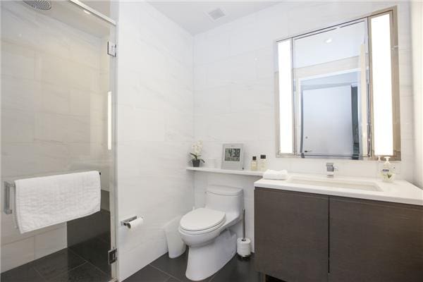 bathroom featuring tile patterned floors, a shower with door, vanity, tile walls, and toilet