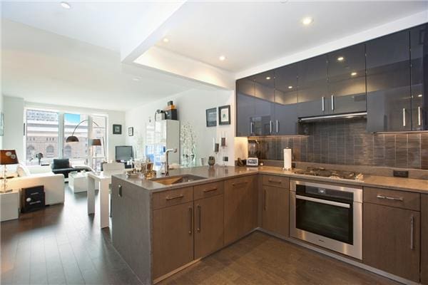 kitchen with dark wood finished floors, stainless steel appliances, open floor plan, a sink, and a peninsula