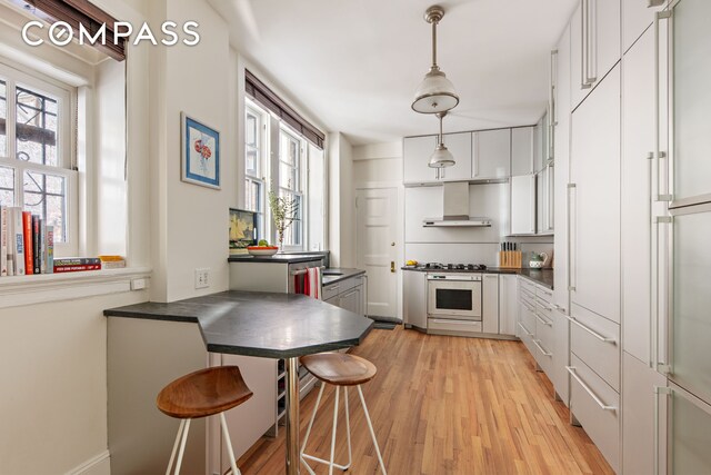 24 Gramercy Park S Unit 1/2E, New York City, NY 10003 - kitchen featuring wall chimney range hood, dark countertops, white gas range oven, and white cabinetry