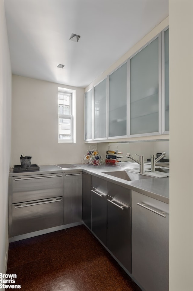 kitchen featuring stainless steel counters, a sink, glass insert cabinets, and modern cabinets