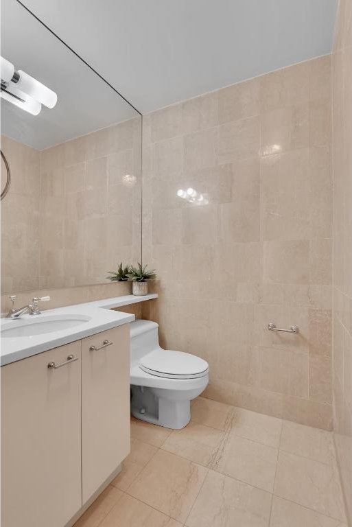 bathroom with tile walls, toilet, vanity, and tile patterned flooring