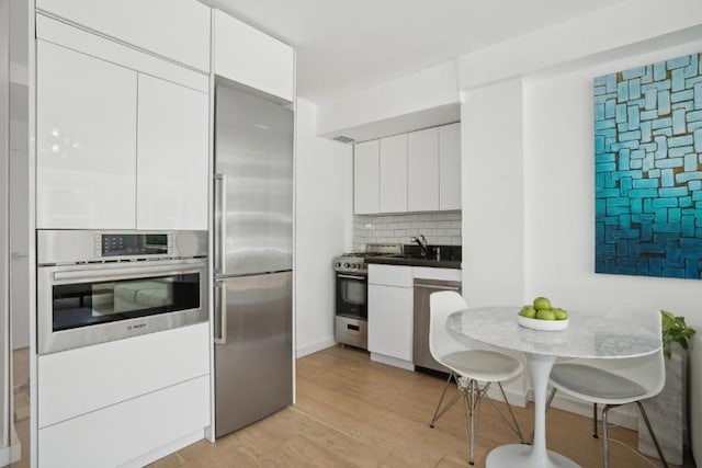 kitchen featuring white cabinetry, backsplash, light hardwood / wood-style flooring, and stainless steel appliances