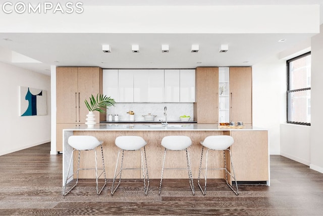 kitchen with white cabinetry, an island with sink, sink, backsplash, and dark hardwood / wood-style floors