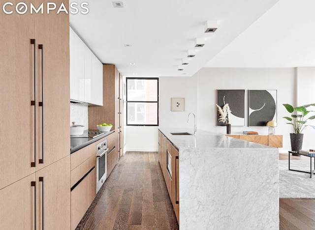 kitchen featuring a spacious island, white cabinets, sink, oven, and black electric cooktop