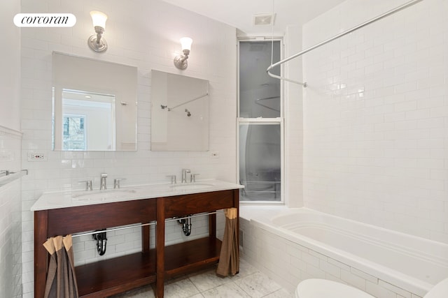 116 E 91st St, New York City, NY 10128 - bathroom featuring tile walls, double vanity, tiled shower / bath, tile patterned floors, and toilet