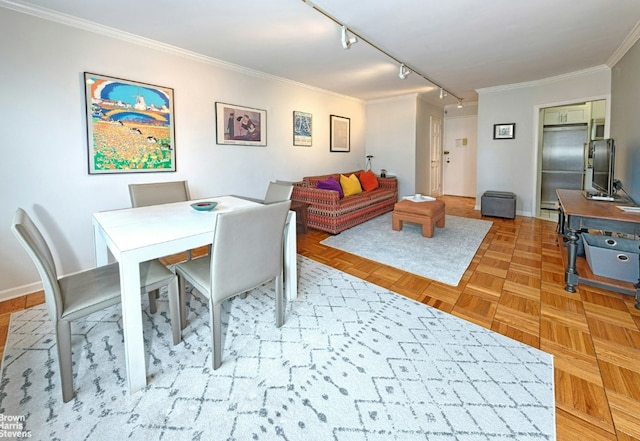 dining room with track lighting, ornamental molding, and light parquet floors