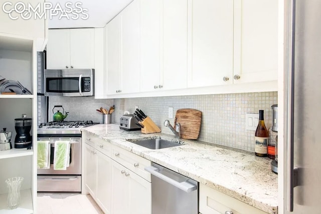 kitchen featuring sink, appliances with stainless steel finishes, white cabinetry, light stone countertops, and decorative backsplash