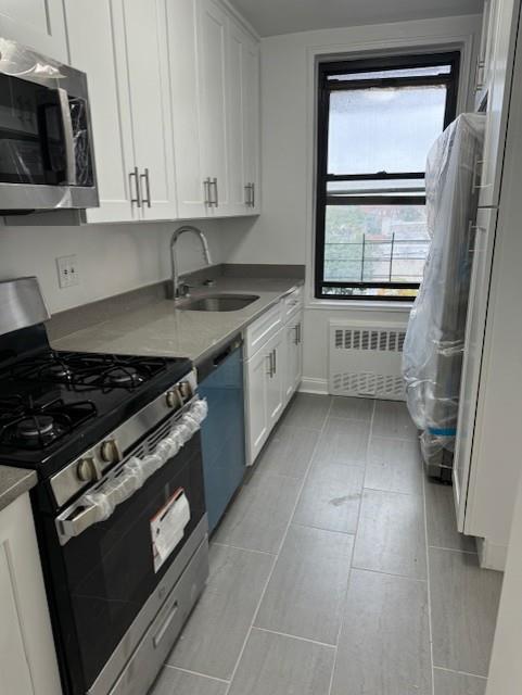 kitchen featuring white cabinets, appliances with stainless steel finishes, radiator, and sink