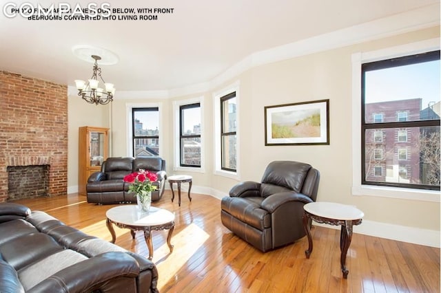 living room with a brick fireplace, ornamental molding, a chandelier, and light wood-type flooring