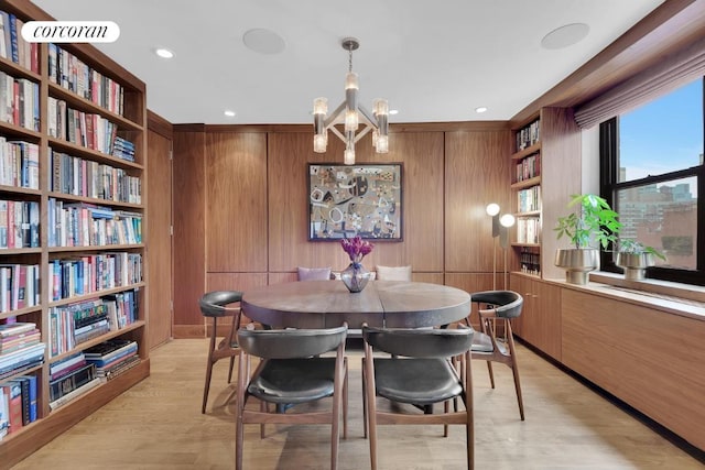 dining room featuring a notable chandelier, light hardwood / wood-style flooring, and wood walls