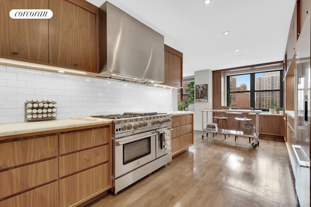 kitchen with decorative backsplash, light wood-type flooring, range with two ovens, and wall chimney range hood