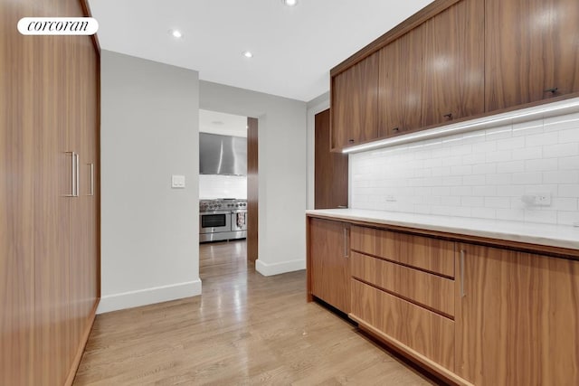 kitchen with range with two ovens, backsplash, light hardwood / wood-style floors, and wall chimney exhaust hood