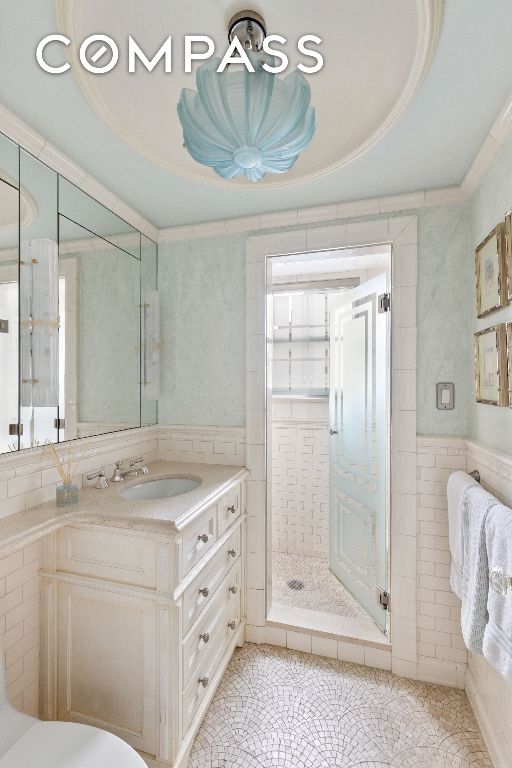 bathroom featuring walk in shower, crown molding, tile walls, vanity, and a raised ceiling