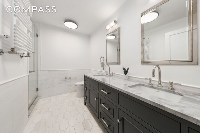 110 W 81st St, New York City, NY 10024 - bathroom featuring a towel warmer, a stall shower, double vanity, tile walls, and toilet