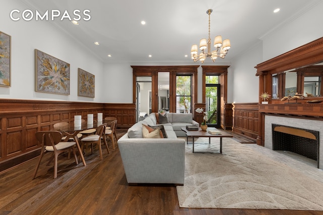 living area with wainscoting, a premium fireplace, ornamental molding, dark wood-style flooring, and an inviting chandelier