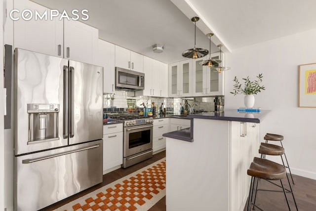 115 E 9th St Unit 8E, New York City, NY 10003 - kitchen with appliances with stainless steel finishes, a peninsula, dark countertops, and glass insert cabinets