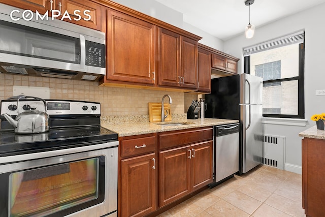 kitchen featuring light stone counters, radiator heating unit, a sink, appliances with stainless steel finishes, and tasteful backsplash