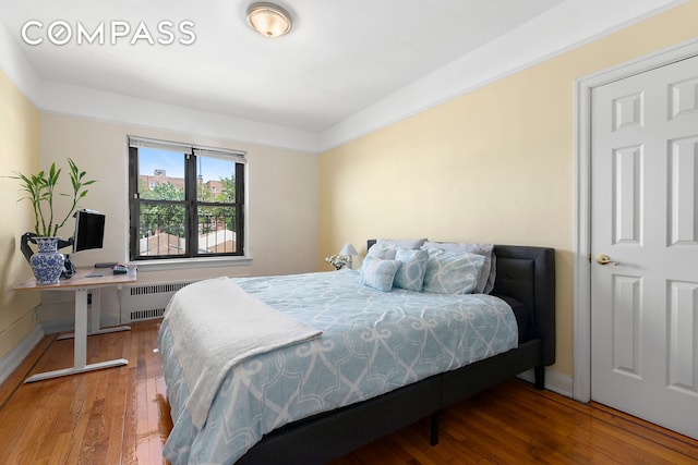 bedroom with baseboards, radiator heating unit, and hardwood / wood-style flooring