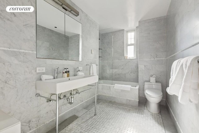 bathroom featuring toilet, tiled shower / bath combo, a sink, tile walls, and tile patterned floors