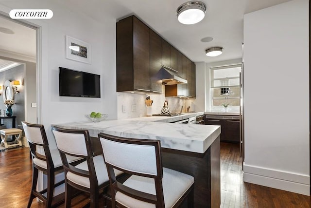 kitchen with a breakfast bar area, light countertops, dark brown cabinetry, a peninsula, and under cabinet range hood