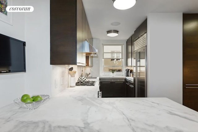 kitchen featuring dark brown cabinetry, light stone countertops, appliances with stainless steel finishes, and wall chimney range hood