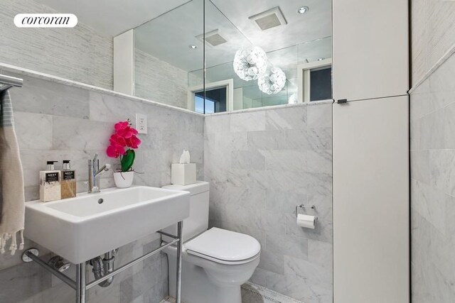 half bath with tile walls, toilet, and a sink