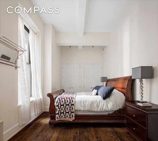 bedroom featuring dark wood-style flooring, beamed ceiling, baseboards, and two closets