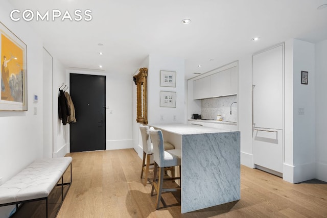 kitchen featuring light wood-type flooring, light countertops, white cabinets, and decorative backsplash