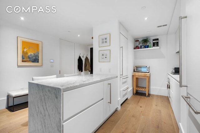 kitchen featuring light stone counters, white cabinetry, visible vents, and light wood finished floors