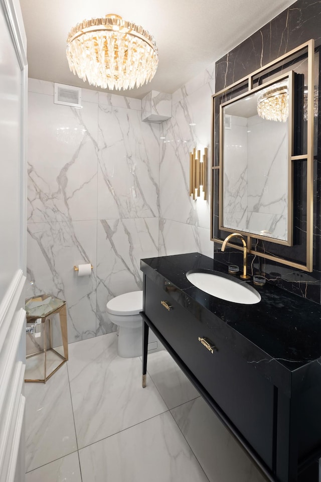 bathroom with visible vents, toilet, marble finish floor, stone wall, and vanity