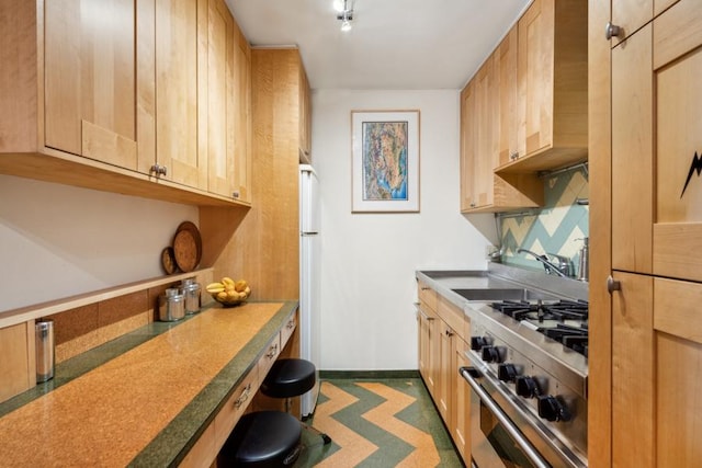 kitchen featuring freestanding refrigerator, light brown cabinets, a sink, high end range, and baseboards