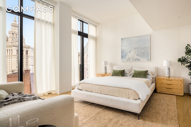 bedroom with baseboards, access to outside, wood finished floors, and a city view