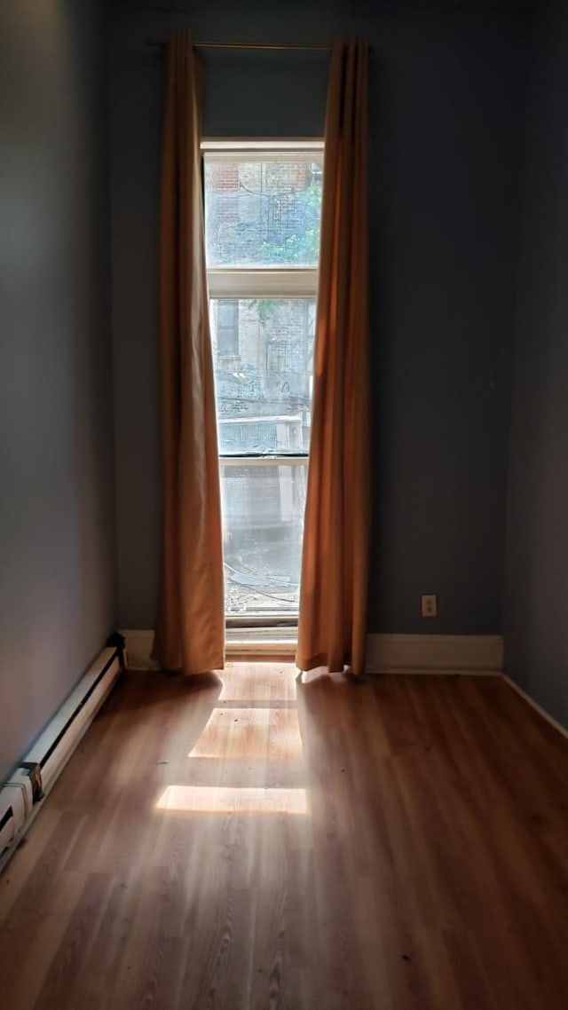 unfurnished room with a baseboard radiator, baseboards, and wood finished floors