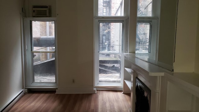 unfurnished living room featuring baseboards, baseboard heating, an AC wall unit, and wood finished floors