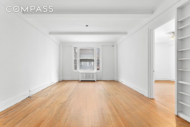 unfurnished room with beam ceiling, built in shelves, radiator heating unit, and wood-type flooring