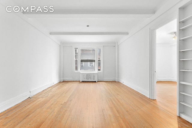 empty room featuring beamed ceiling, radiator, hardwood / wood-style floors, and built in features