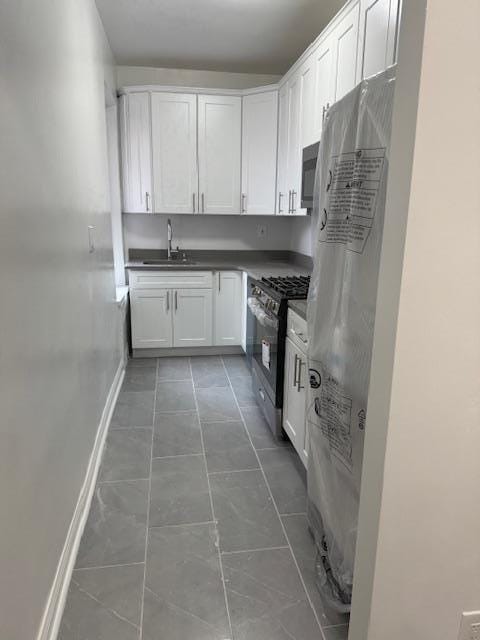 kitchen with stainless steel gas stove, fridge, white cabinetry, and sink